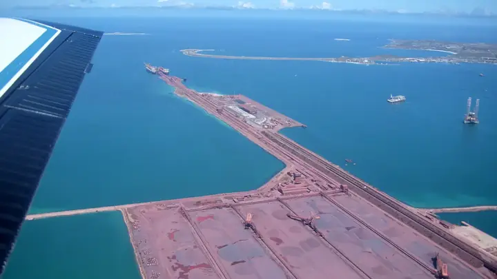 Aerial view of iron ore stockpiles, stacking machines and a long ore jetty with ships berthed at the Port of Saldanha